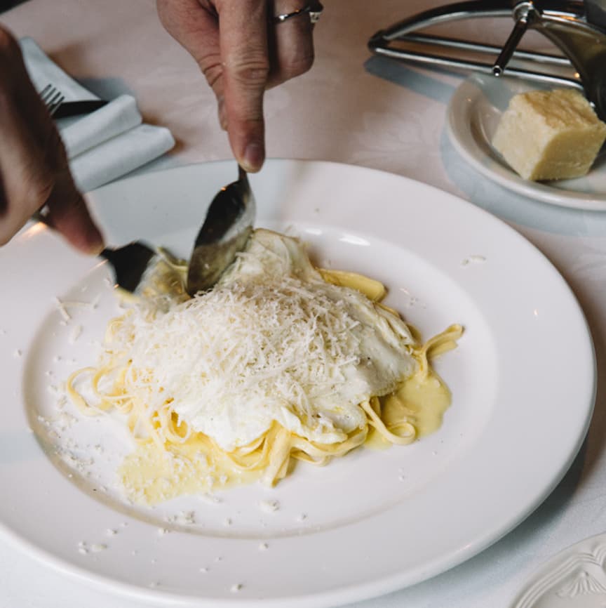 Parmesan being shaved over a creamy pasta dish at the table